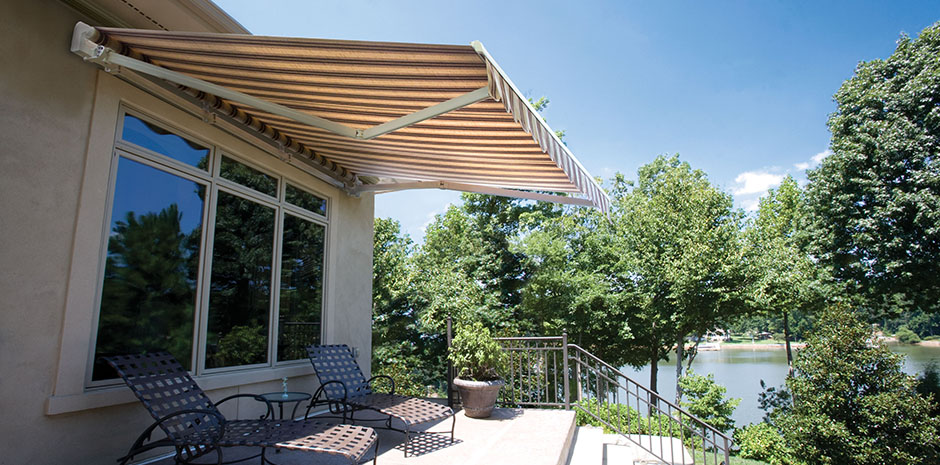 striped motorized outdoor shade covering patio chairs next to a lake with trees